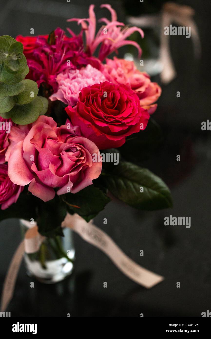 Bouquet rose avec eucalyptus dans un vase en verre sur une surface réfléchissante sombre Banque D'Images
