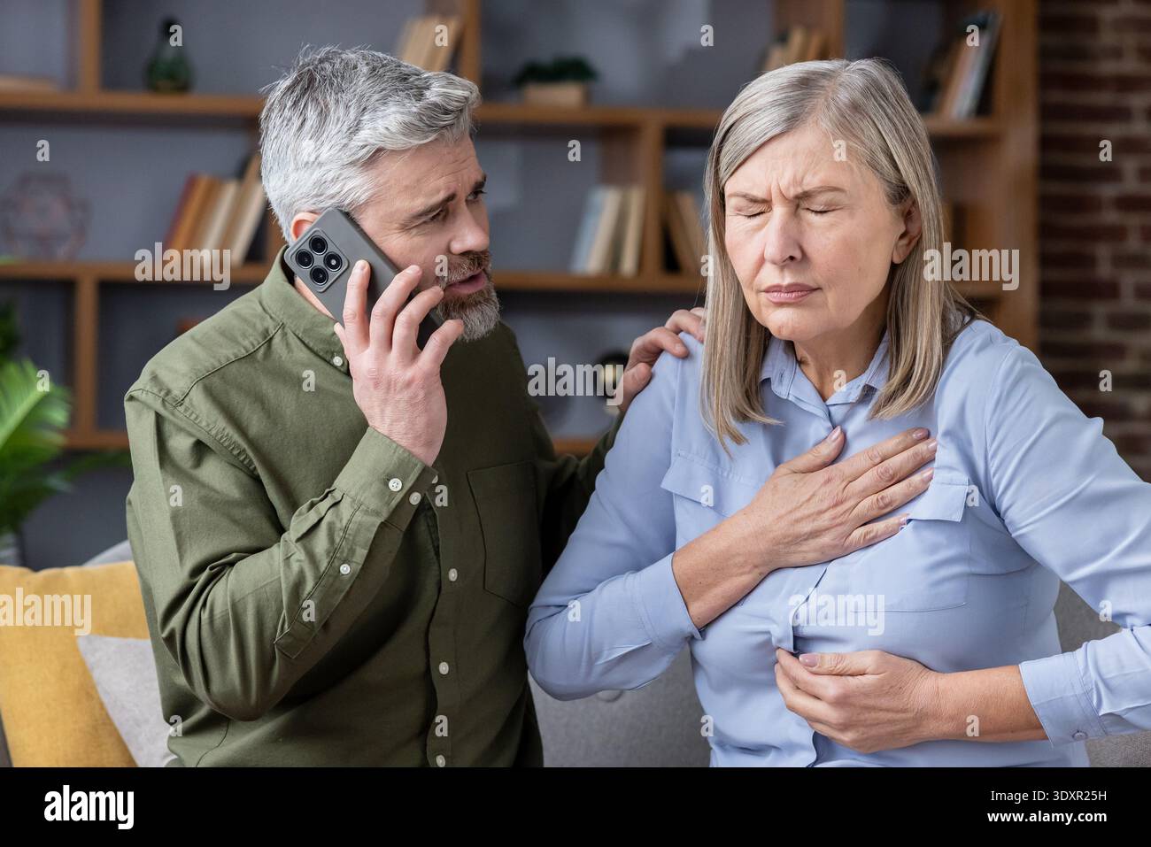 Un homme concerné compose les services d'urgence tandis que son partenaire âgé serre sa poitrine en raison de douleurs sévères à la maison, d'une crise médicale urgente et d'un soutien en cas de détresse Banque D'Images