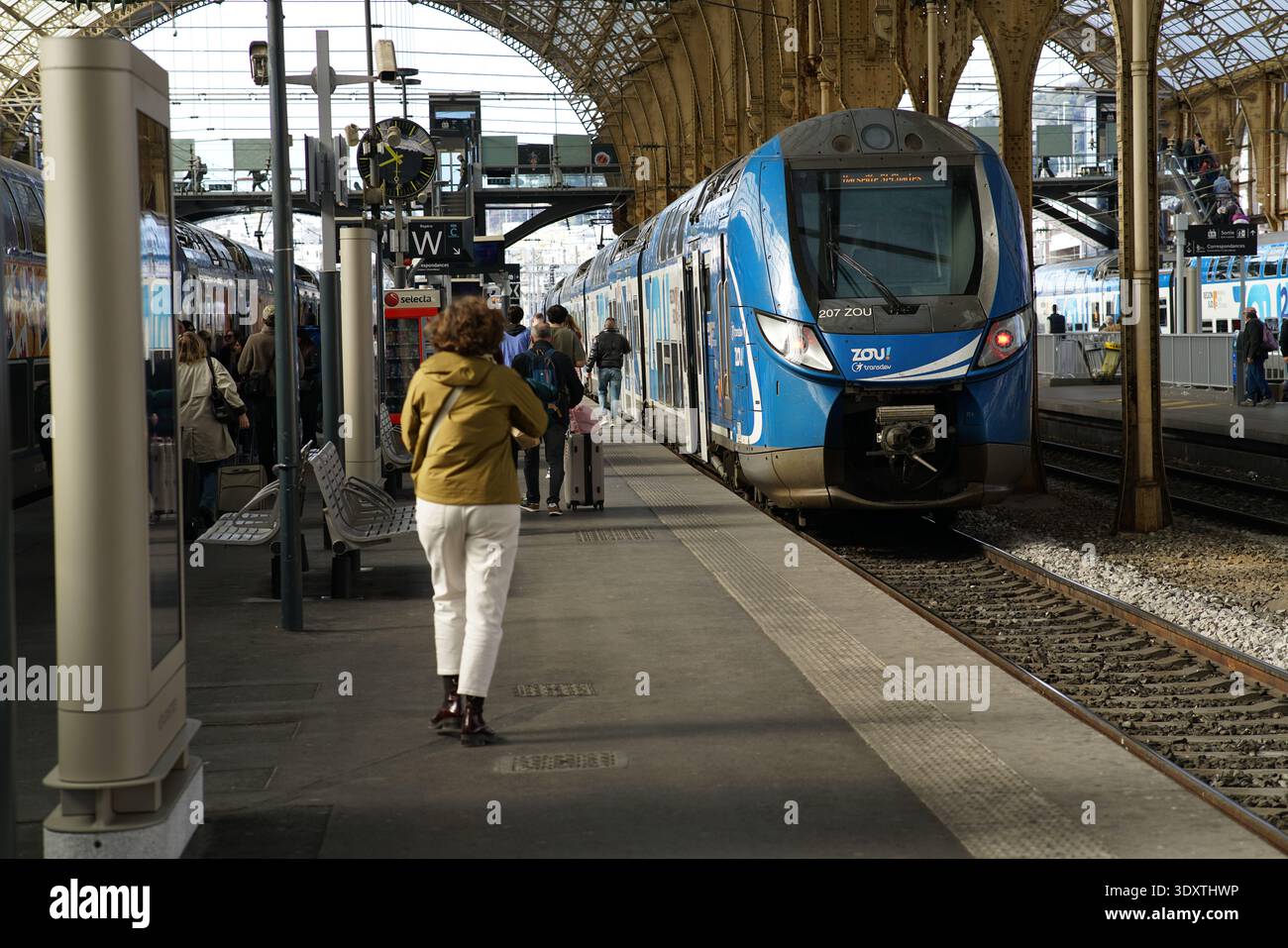 Train régional Blue Zou à la plate-forme historique Gare de Nice ville pendant que les passagers attendent et une femme en veste jaune marche le long du bord.Nice, France Banque D'Images