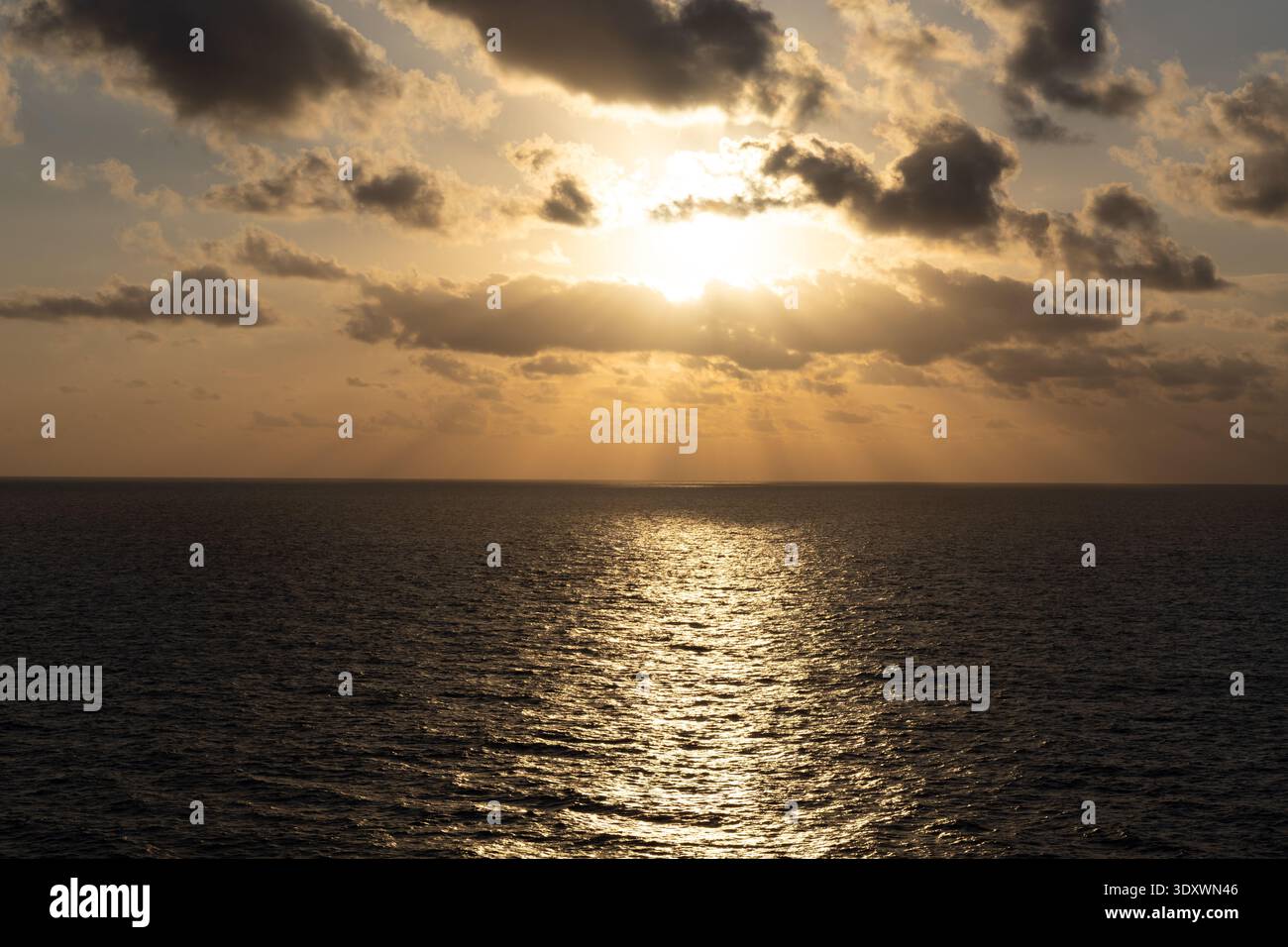 Lever de soleil doré sur l'océan calme avec des nuages spectaculaires et la lumière du soleil se reflétant à travers l'horizon de la mer ouverte. Banque D'Images