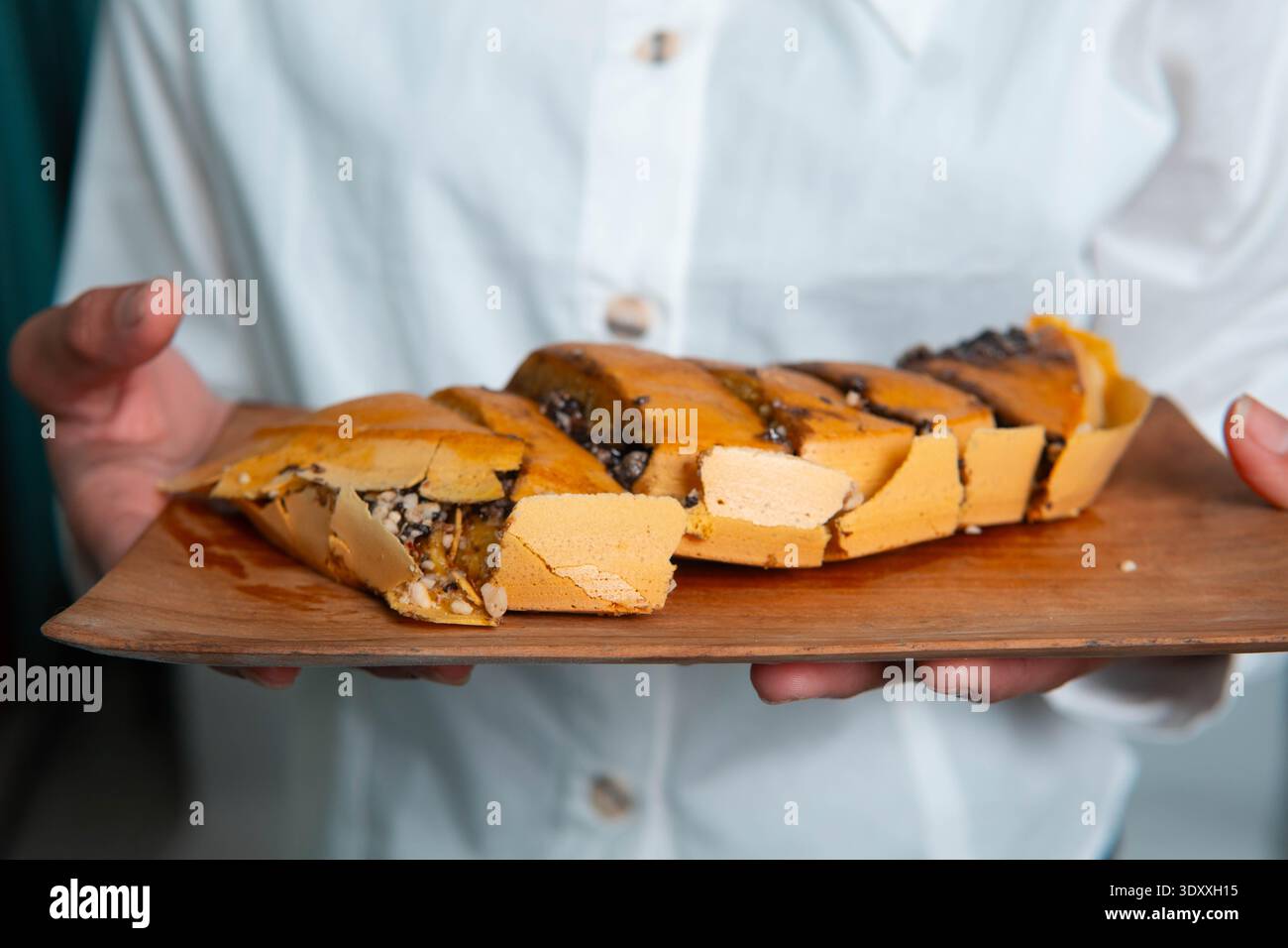 Vue latérale rapprochée de Martabak Manis tranché sur une assiette en bois, montrant une texture épaisse et une garniture de chocolat fondu sur un fond à motifs. Banque D'Images