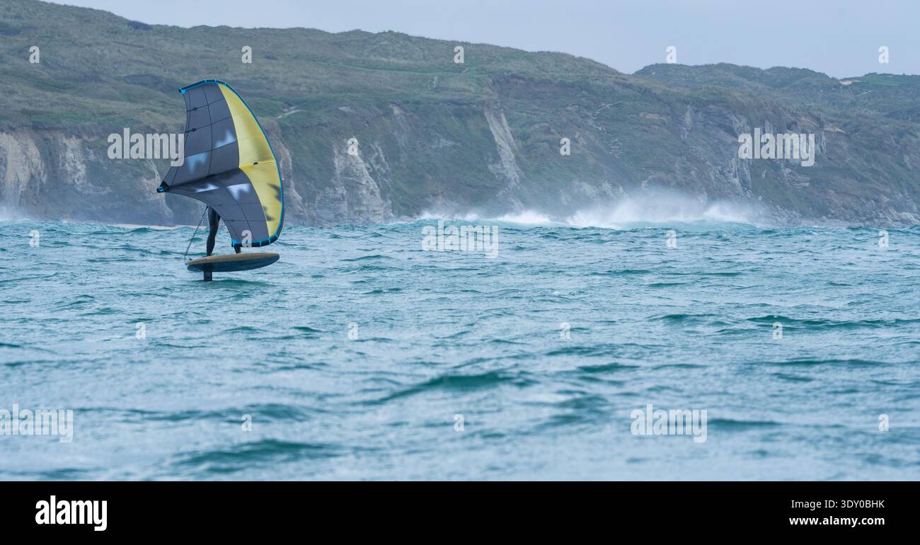 Une aile d'homme défile en mer à l'aide d'une aile gonflable à main jaune et grise, chevauchant une planche de surf hydrofoil. Mer verte, ciel bleu nuageux. Falaises côtières Banque D'Images