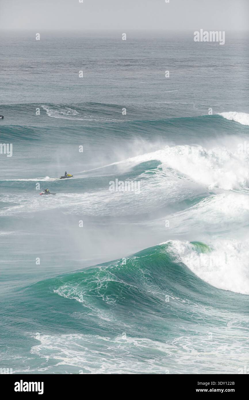 Les surfeurs surfent sur les vagues de l'océan massives avec grâce. La mousse s'écrase alors que les vagues vertes-bleues déferlent vers l'avant. Un surfeur se tient prêt, un autre disparaît en spr blanc Banque D'Images