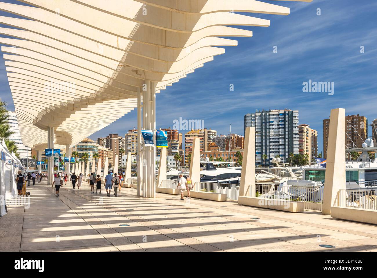 Malaga, Espagne - 12 septembre 2024 : passerelle moderne donnant sur une marina, ombragée par une verrière architecturale unique. Les gens se promènent le long du promen ensoleillé Banque D'Images