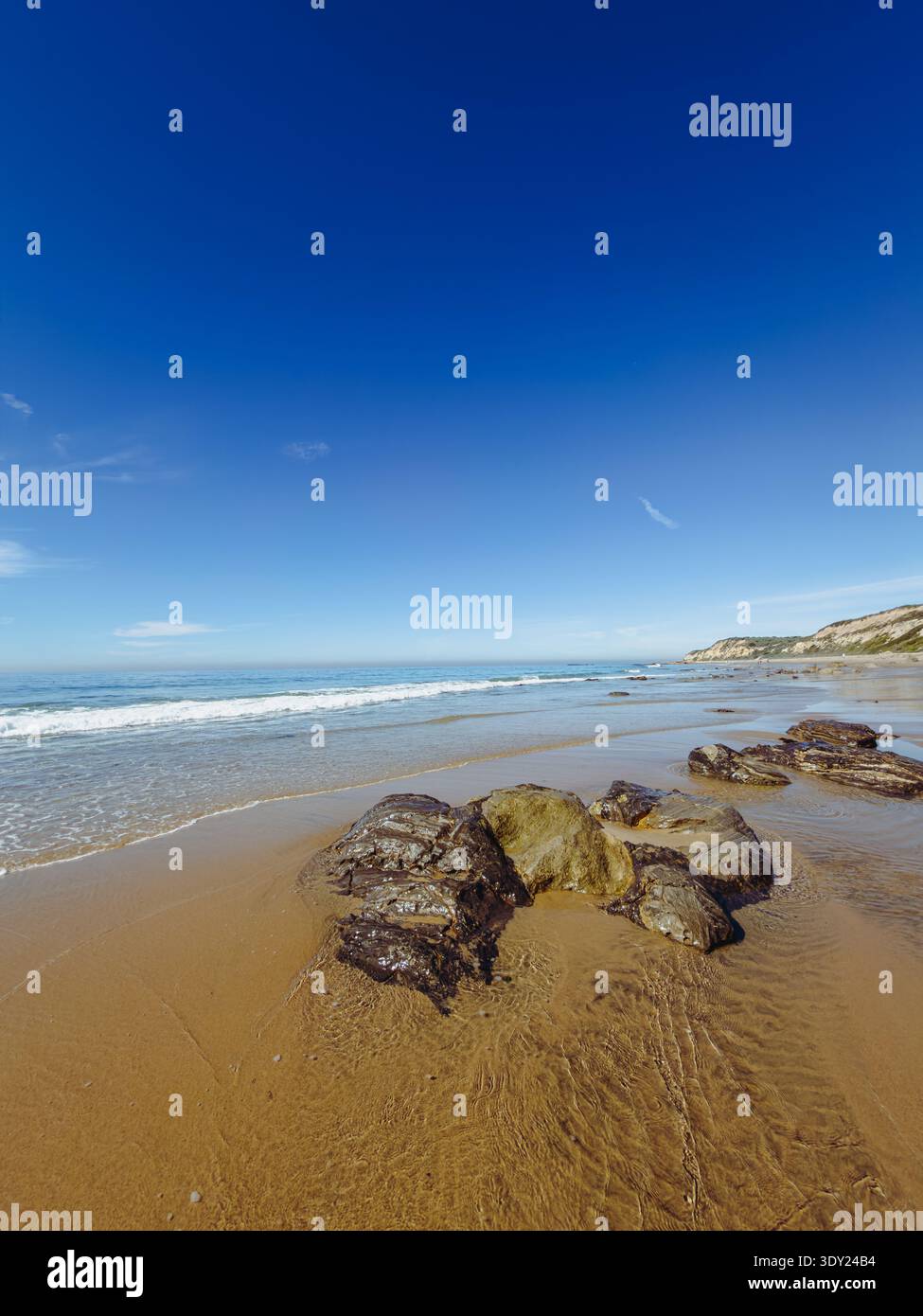 Plage de sable avec quelques gros rochers par une journée ensoleillée avec des vagues se lavant jusqu'au rivage Banque D'Images