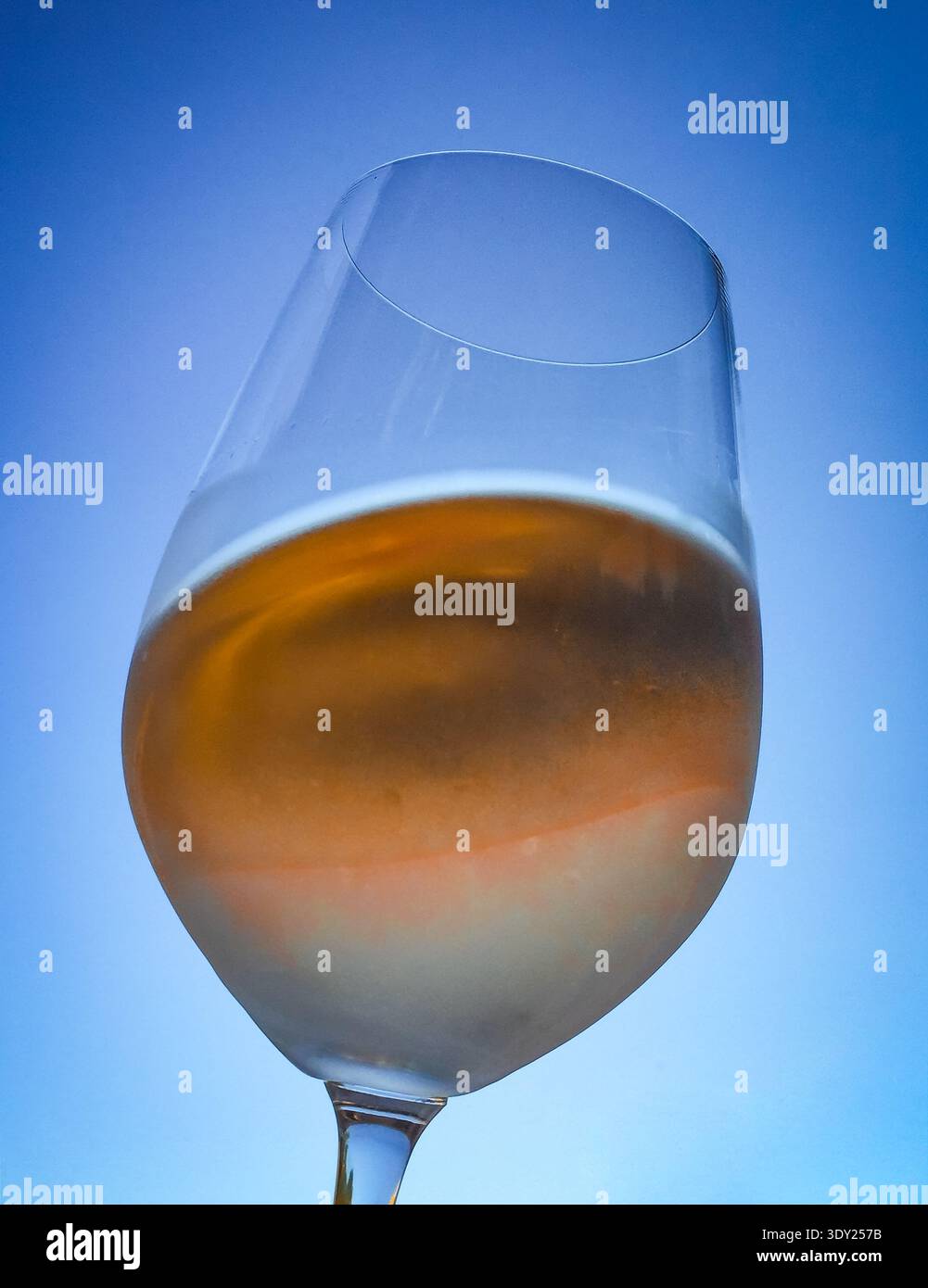 Gros plan d'un élégant verre de vin rosé capturé à l'extérieur avec un ciel bleu vif en toile de fond. Banque D'Images