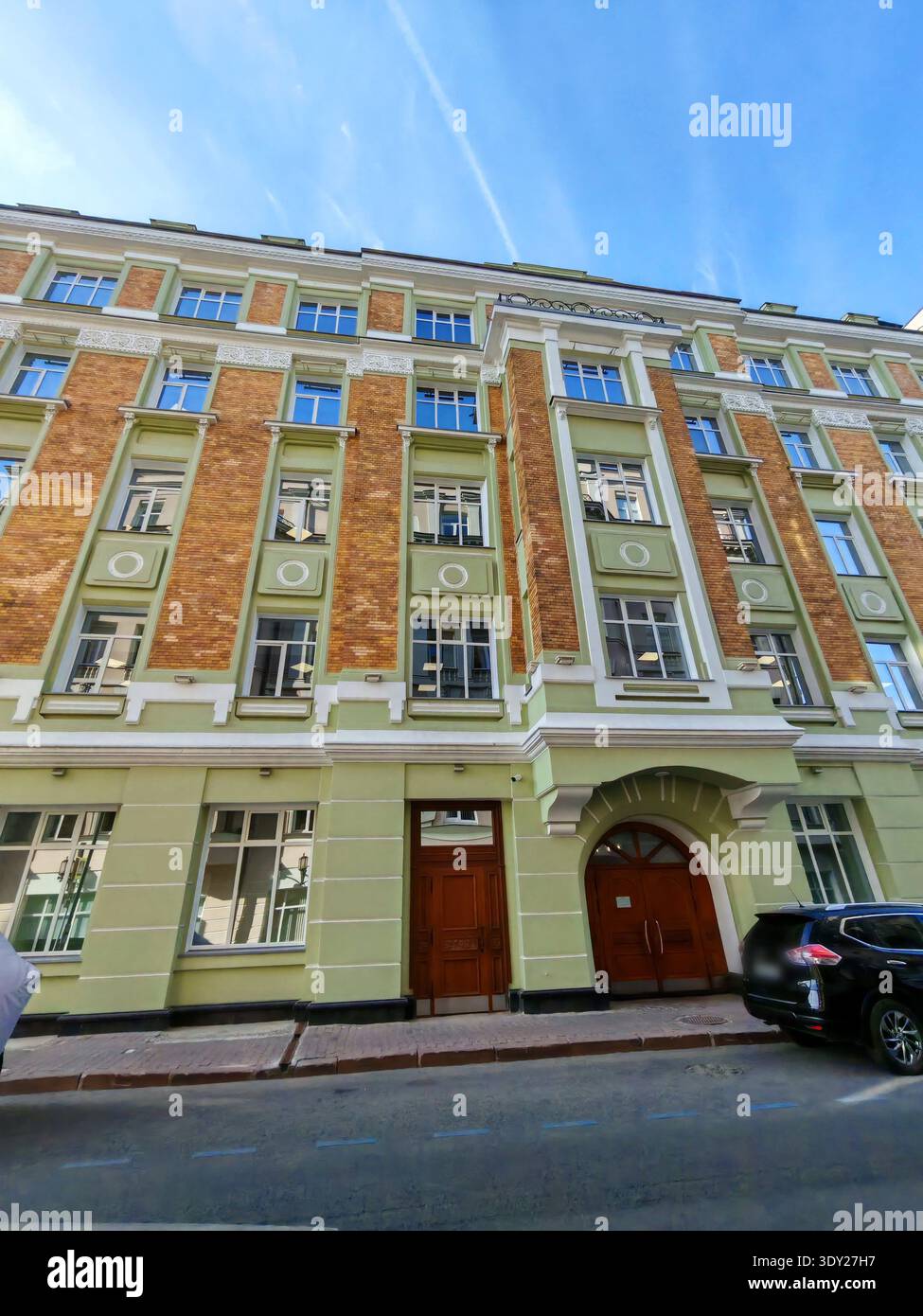 Un bâtiment urbain jaune vif avec une fenêtre circulaire et un design de façade propre, encadré par des arbres verts et des clôtures métalliques. L'image met l'accent sur la modernité Banque D'Images