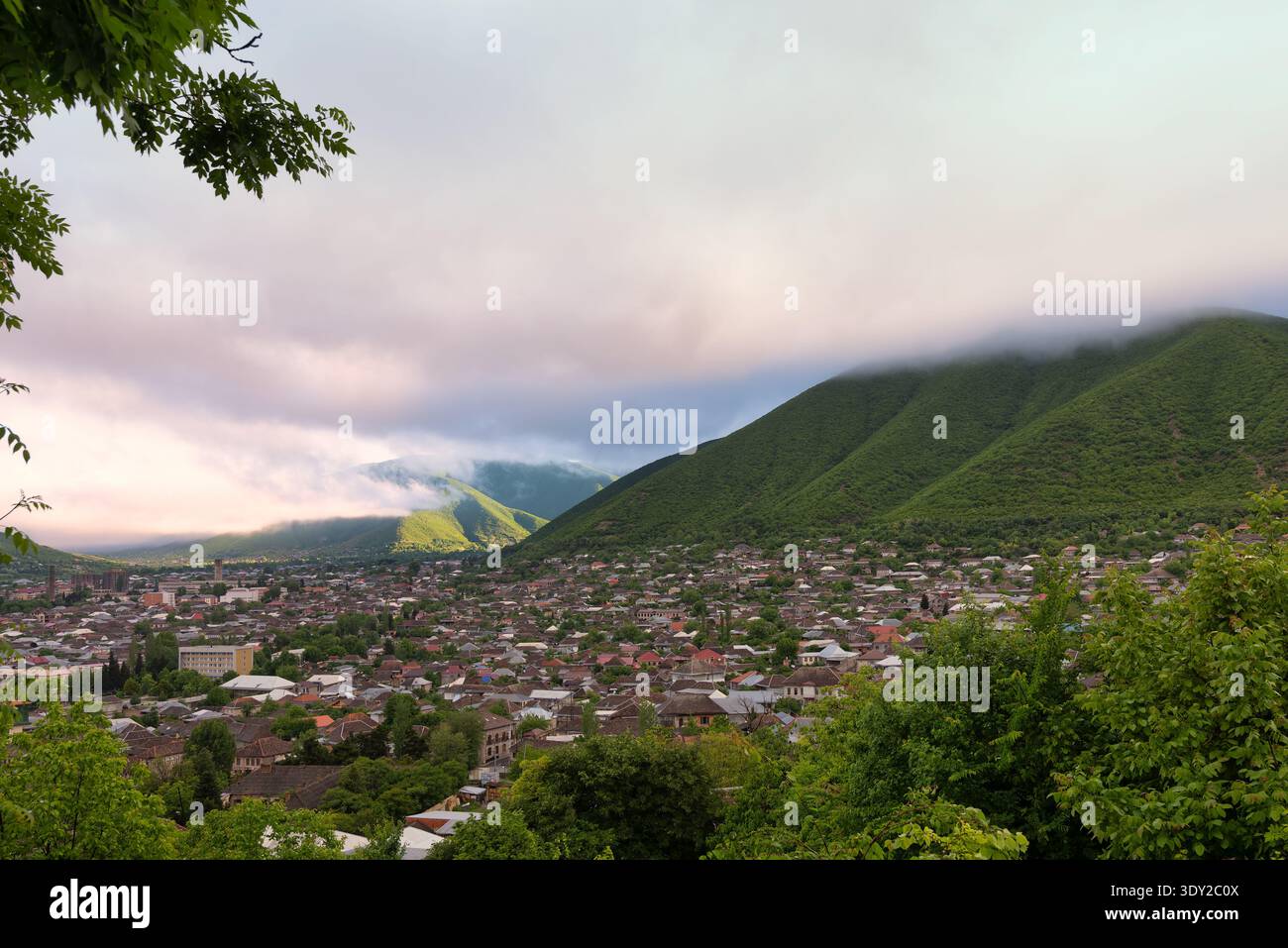Ville de Shaki, Azerbaïdjan, nichée dans une vallée aux montagnes vertes partiellement couvertes de nuages atmosphériques. Vue aérienne des maisons et des arbres sous un ciel mou Banque D'Images