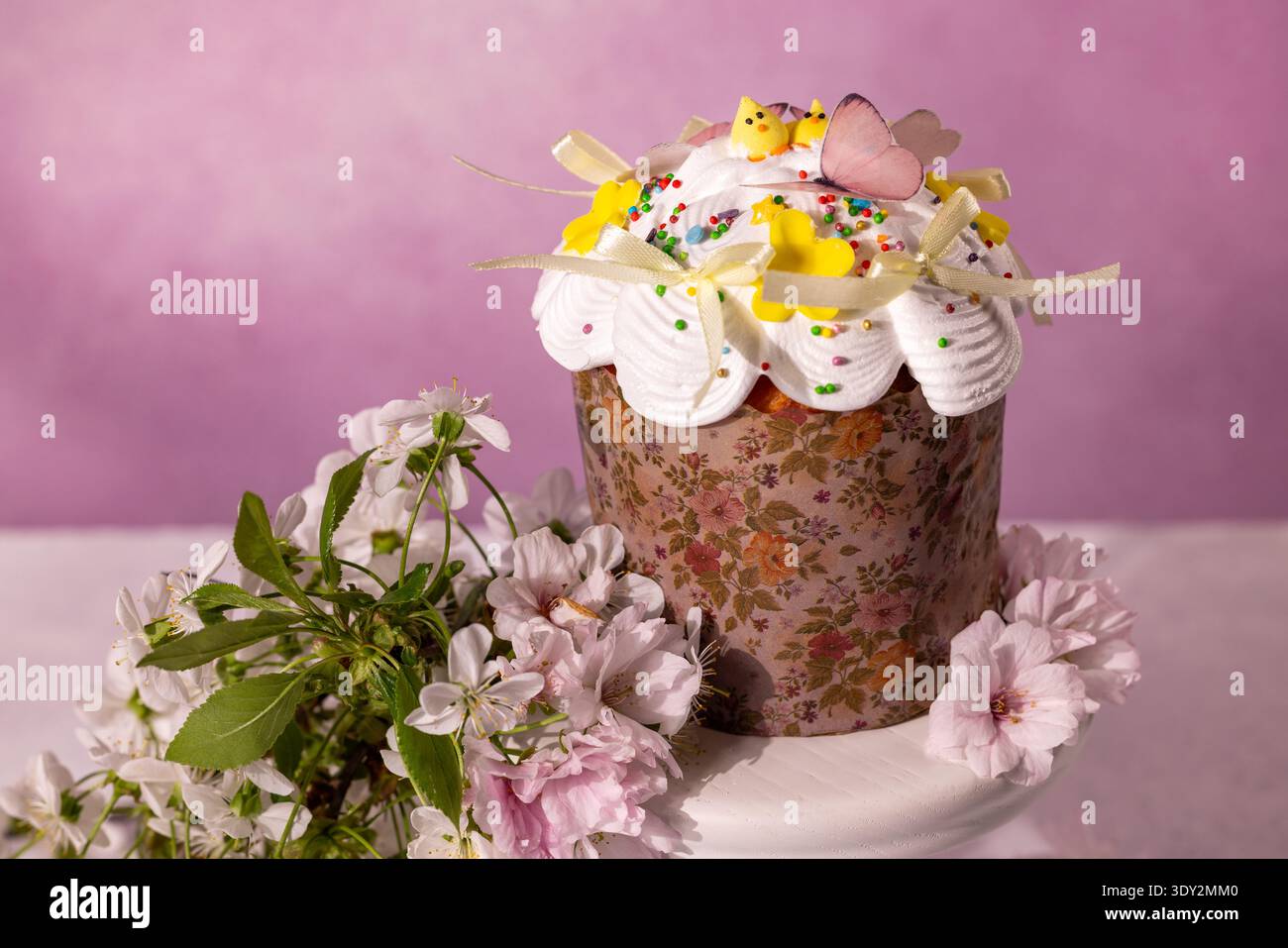 Kulich traditionnel de pâques avec glaçage blanc, saupoudrages colorés et poussins décoratifs, lapins et papillons, arrangé avec délicate fleur de cerisier Banque D'Images