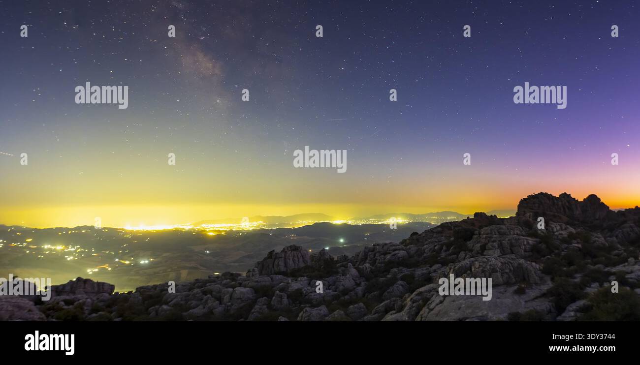 Paysage nocturne panoramique de terrain rocheux sous un ciel étoilé, avec la voie lactée et la lueur urbaine lointaine de la région de Malaga Banque D'Images