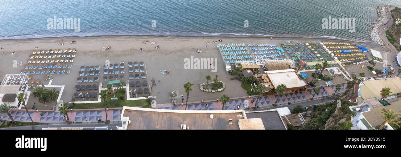Panorama aérien d'une plage de sable dans la région de Malaga-Torremolinos avec des rangées de chaises longues colorées, des parasols, des palmiers et des eaux de mer calmes le long Banque D'Images