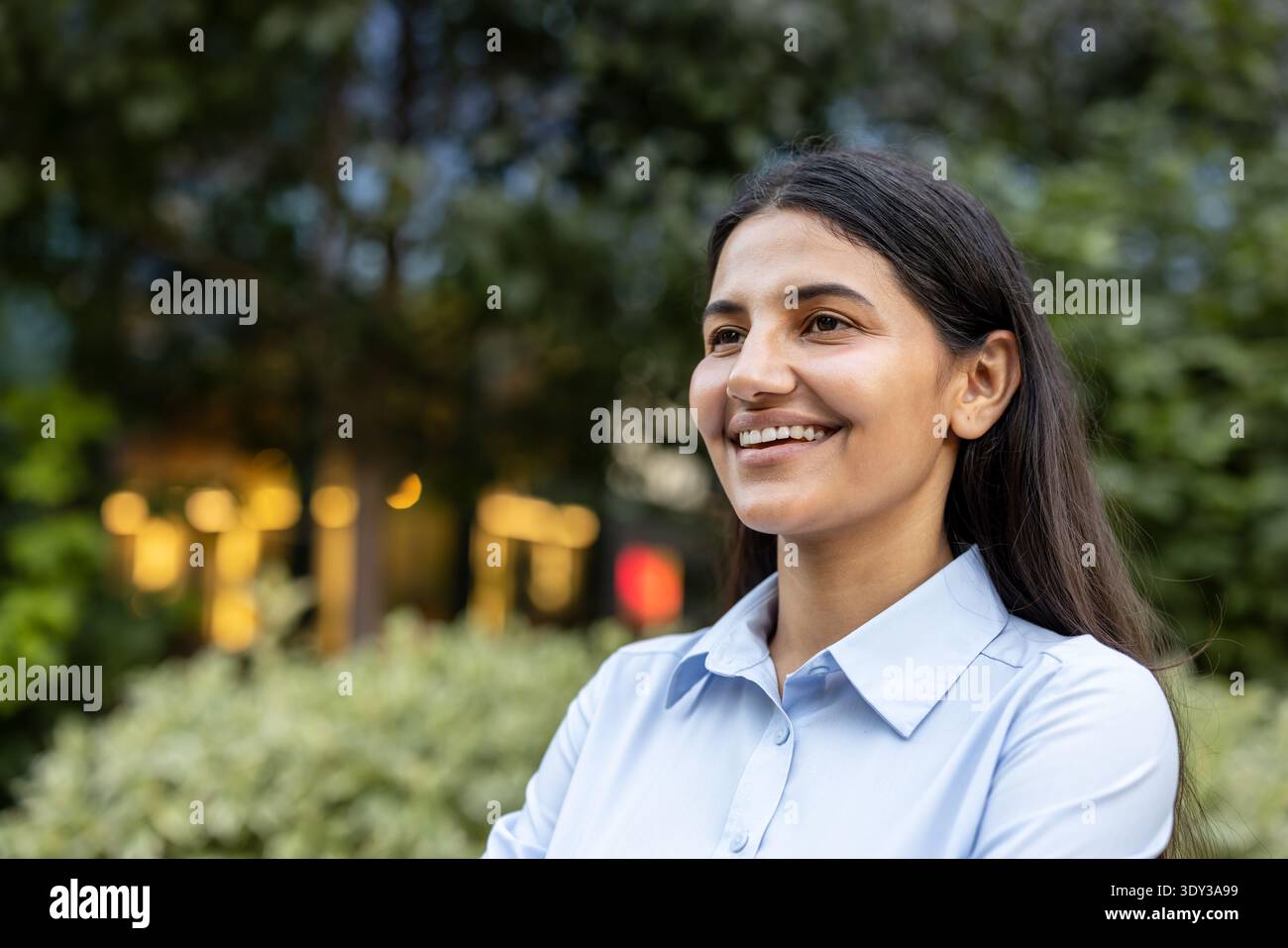 Jeune femme d'affaires indienne souriante et détournée, profitant d'une pause en plein air paisible dans un parc de la ville, confiante et rafraîchie pendant une pause de travail de jour Banque D'Images