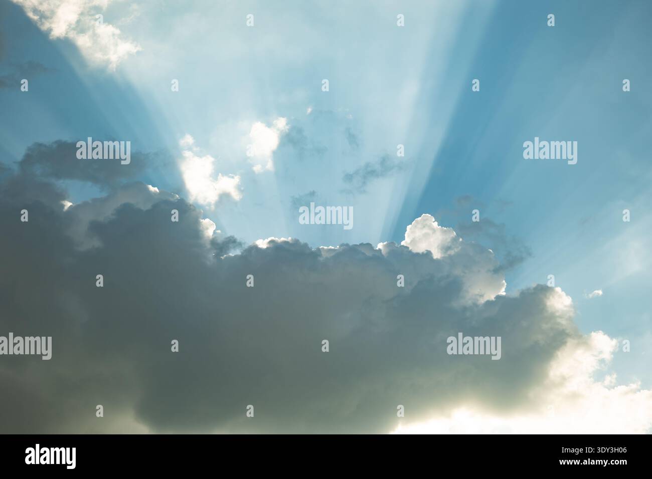 Rayons de soleil perçant à travers les nuages de cumulus sombres créant des rayons lumineux brillants dans le ciel bleu Banque D'Images