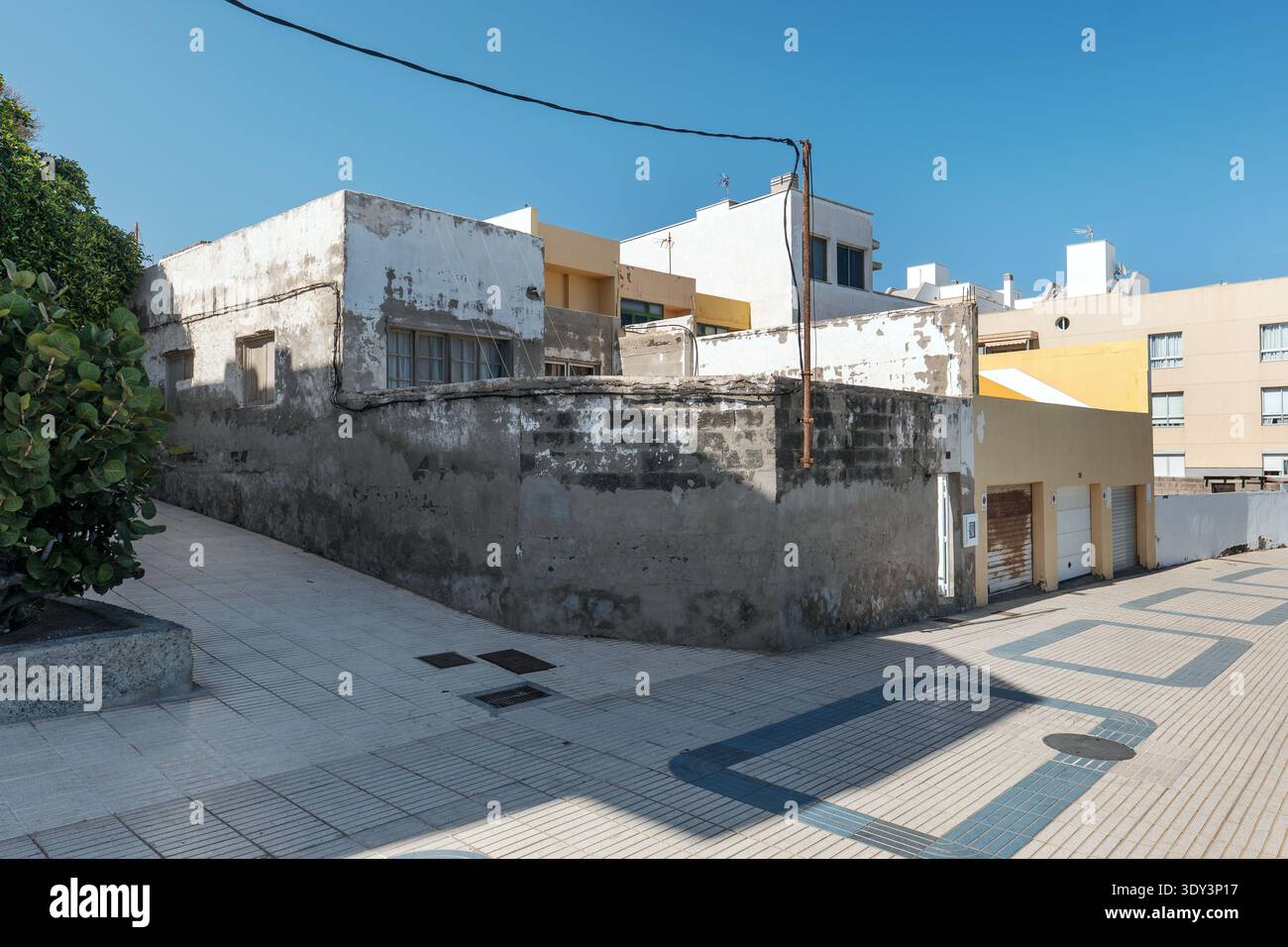Une scène de rue en Espagne avec plusieurs bâtiments, y compris une maison d'angle usée nécessitant une rénovation, situé le long d'une passerelle piétonne carrelée par une journée ensoleillée. Banque D'Images