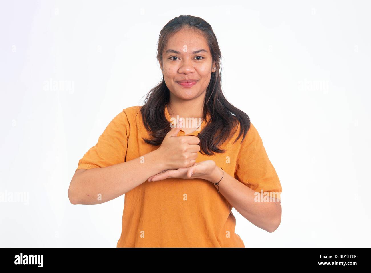Portrait d'une jeune femme indonésienne en chemise orange utilisant le langage des signes pour effectuer le geste pour « aide », isolé sur un fond blanc Uni. Banque D'Images