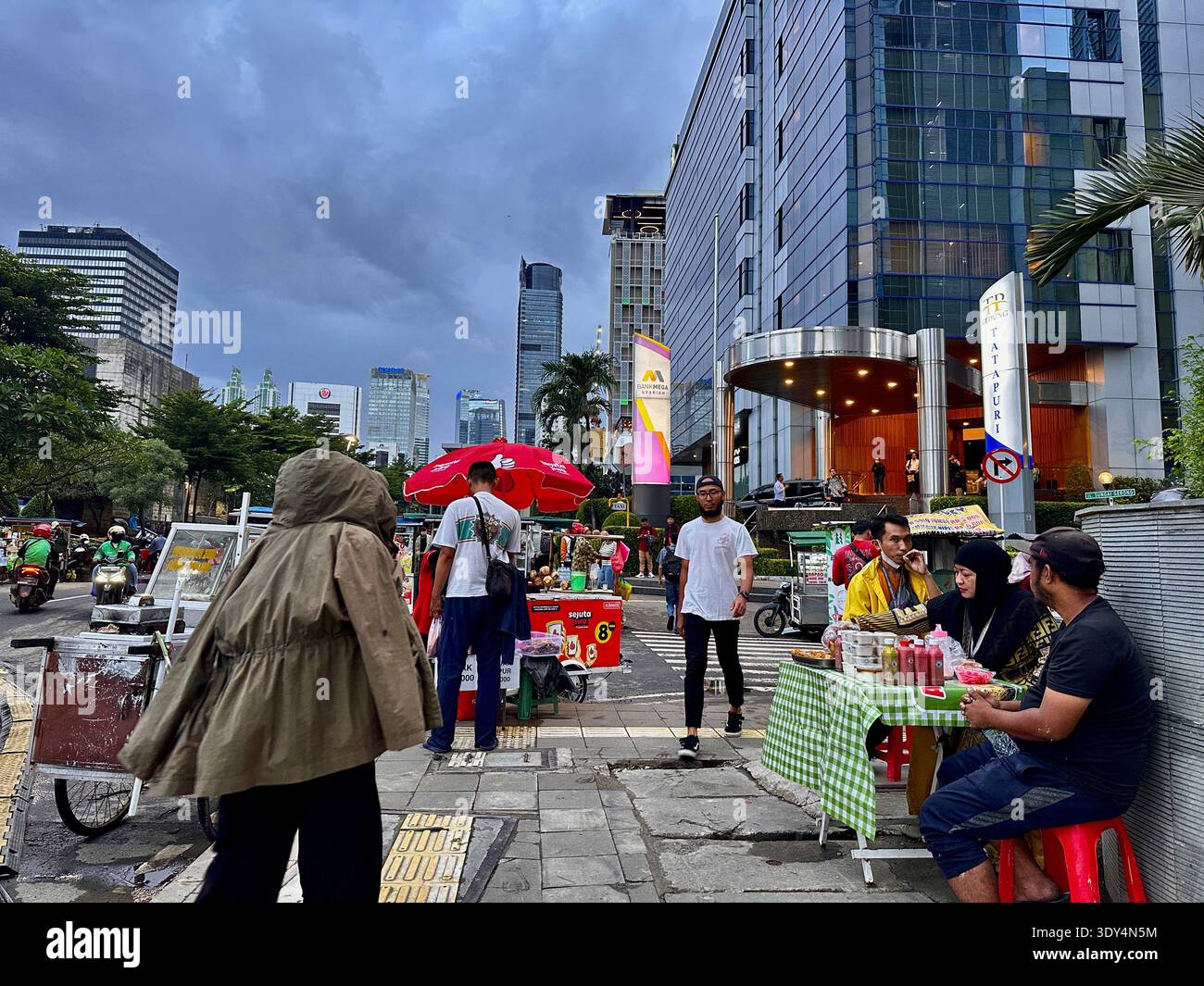 Jakarta - 5 mars 2026 : vendeurs de nourriture de rue et piétons se rassemblent près de la circulation et des tours de bureaux dans une scène nocturne animée près de Bundaran HI. - Image de stock capturée avec un smartphone