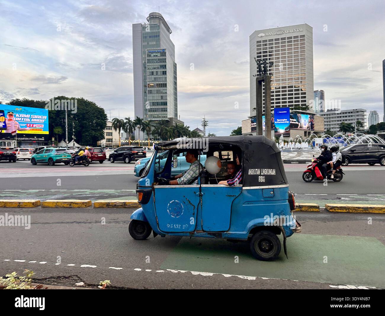 Jakarta - 5 mars 2026 : Un pousse-pousse automatique bajaj bleu transporte des passagers le long d'une avenue animée près de Bundaran HI au crépuscule. - Image de stock capturée avec un smartphone