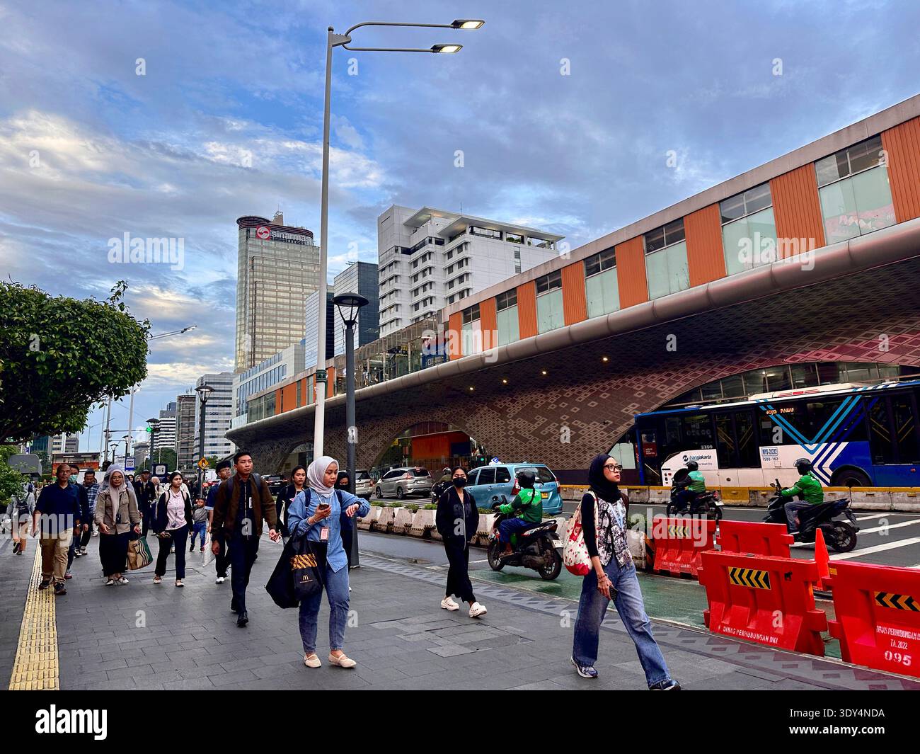 Jakarta, Indonésie - 5 mars 2026 : les navetteurs marchent le long d'un trottoir animé à côté des bus et des motos dans le centre de Jakarta pendant l'heure de pointe du soir. - Image de stock capturée avec un smartphone