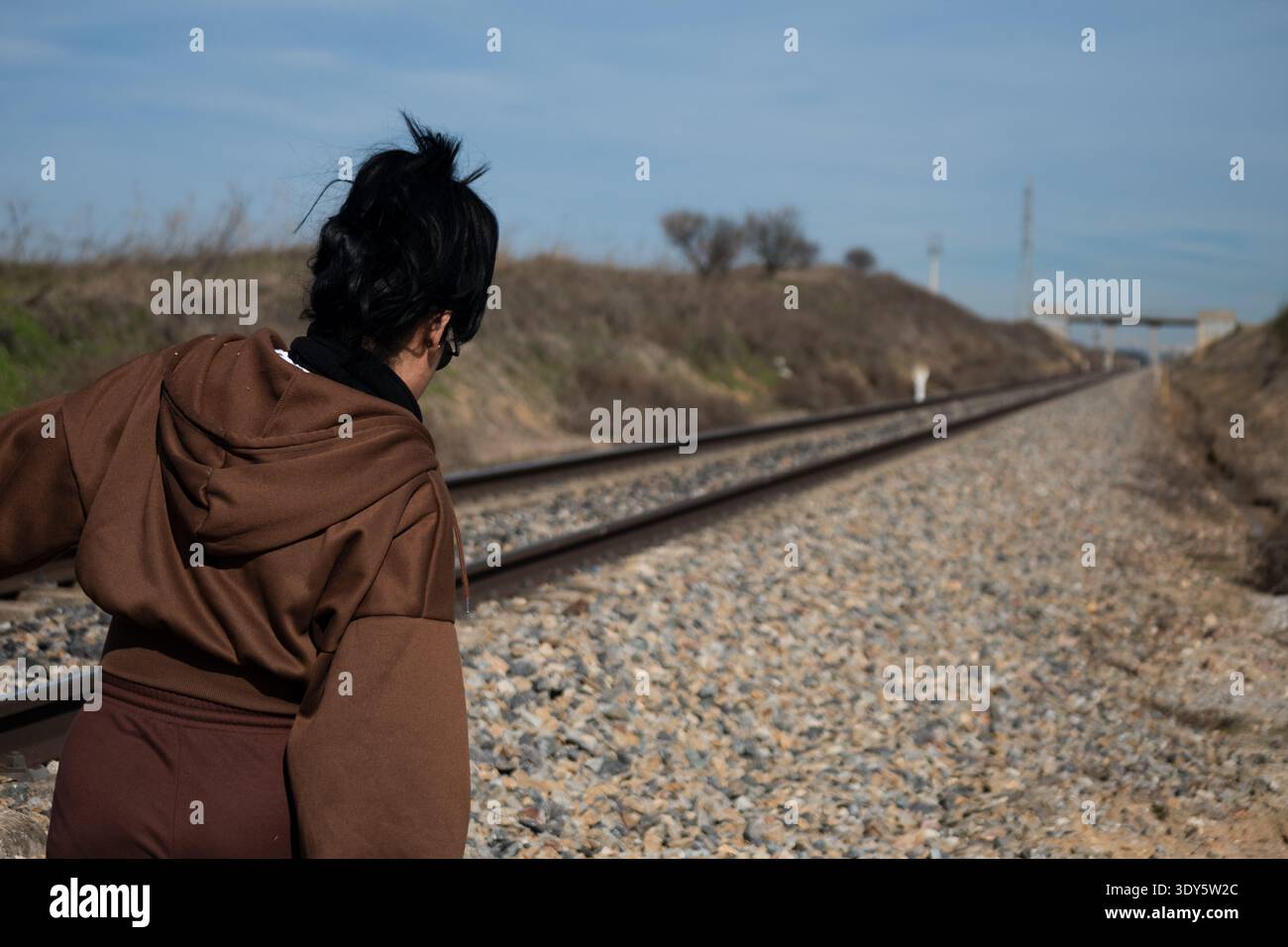 Femme debout près des voies ferrées, regardant au loin, symbolisant le voyage et la solitude Banque D'Images