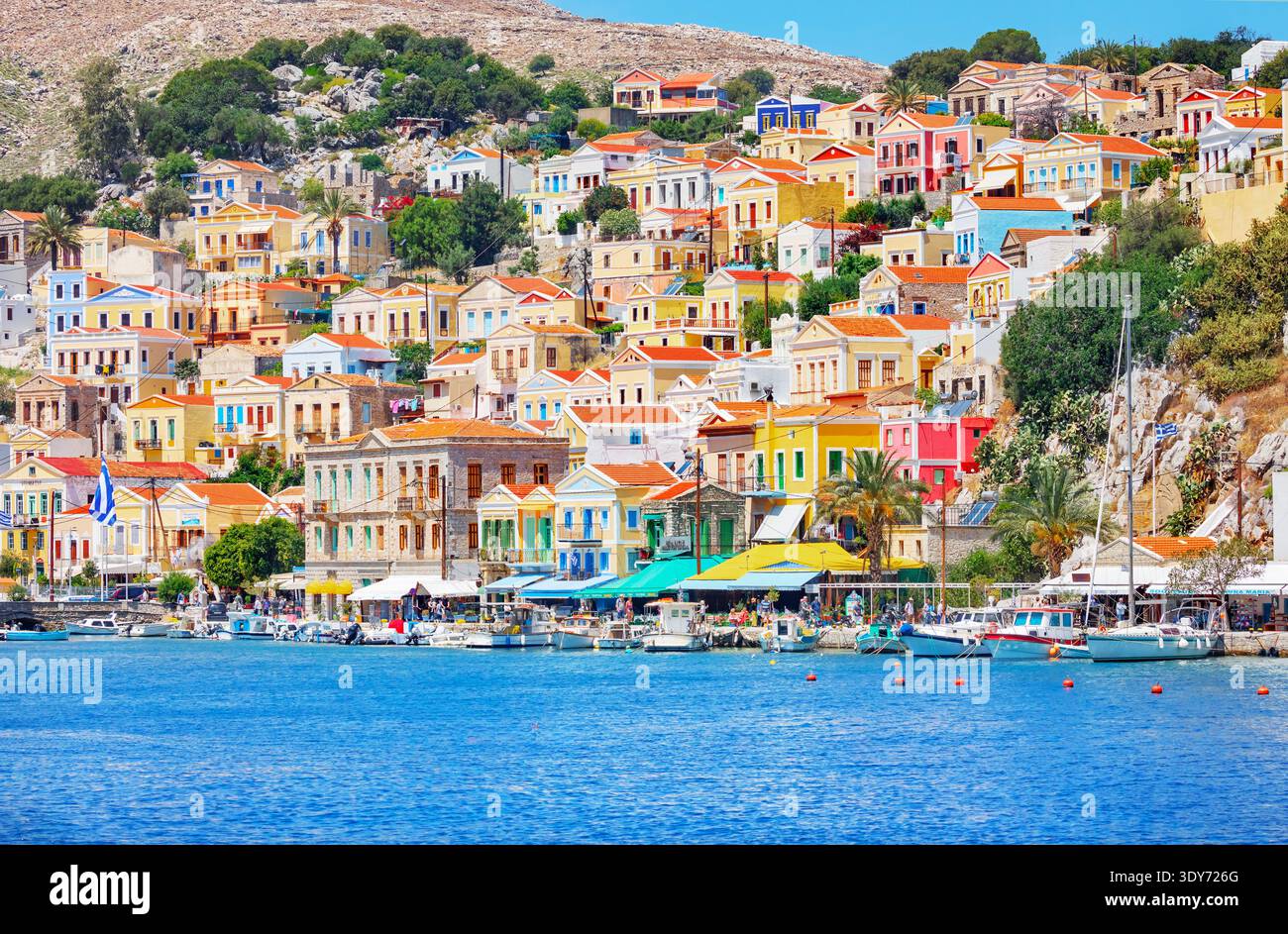 Les bâtiments colorés bordant le port de Symi se reflètent dans l'eau sous un ciel clair sur l'île de Symi, en Grèce Banque D'Images