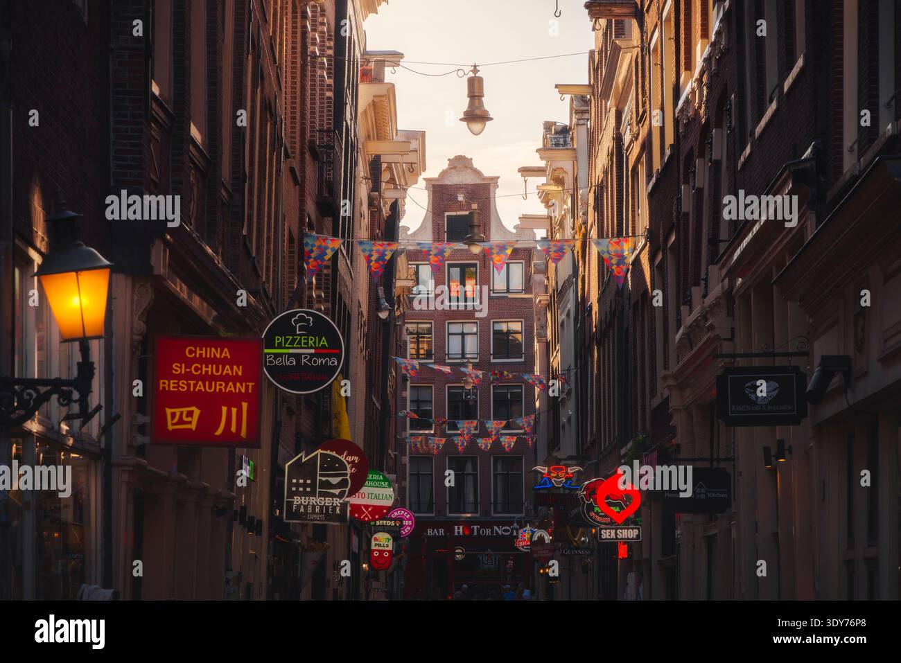 Vue des chaudes lumières du coucher de soleil dans les rues du quartier rouge d'Amsterdam avec des panneaux lumineux et une énergie animée Banque D'Images