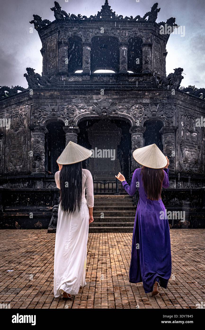 Les femmes en robes traditionnelles ao dai visitent un mausolée historique dans le centre du Vietnam un jour de pluie Banque D'Images