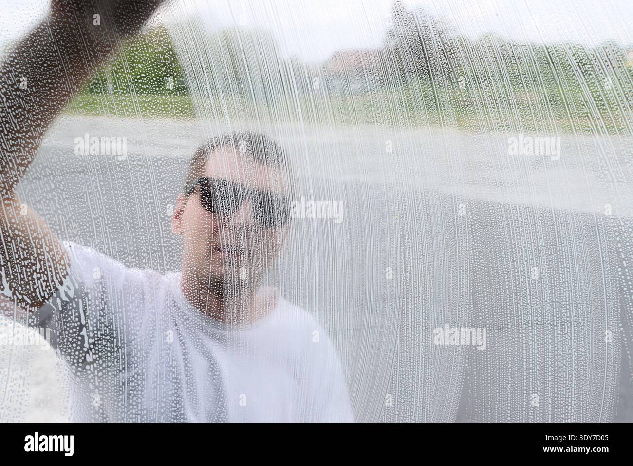 Un homme lave le verre d'un camion, vu à travers la mousse savonneuse. Banque D'Images