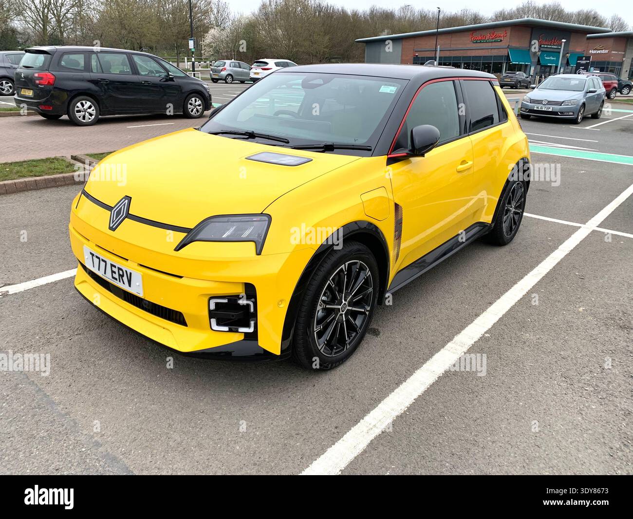 Renault 5 à hayon jaune vif garé dans un parking public montrant sa refonte moderne avec des garnitures noires et un style sportif à Northampton en Angleterre - Image de stock capturée avec un smartphone