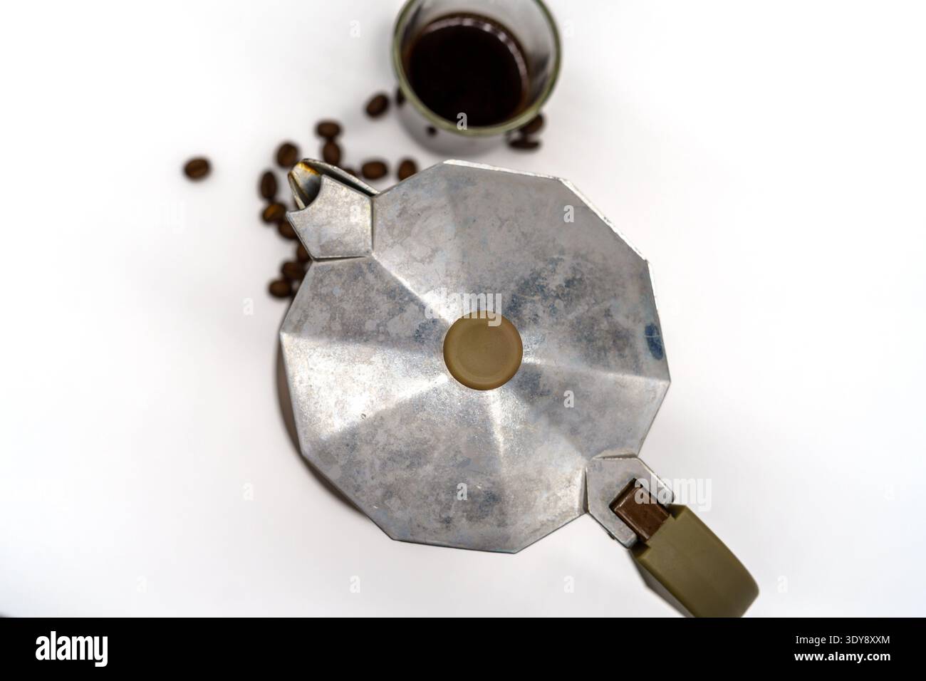 Vue de haut en bas d'un pot de moka argenté sur un fond blanc avec des grains de café dispersés et une tasse de café infusé, composition minimale lumineuse Banque D'Images