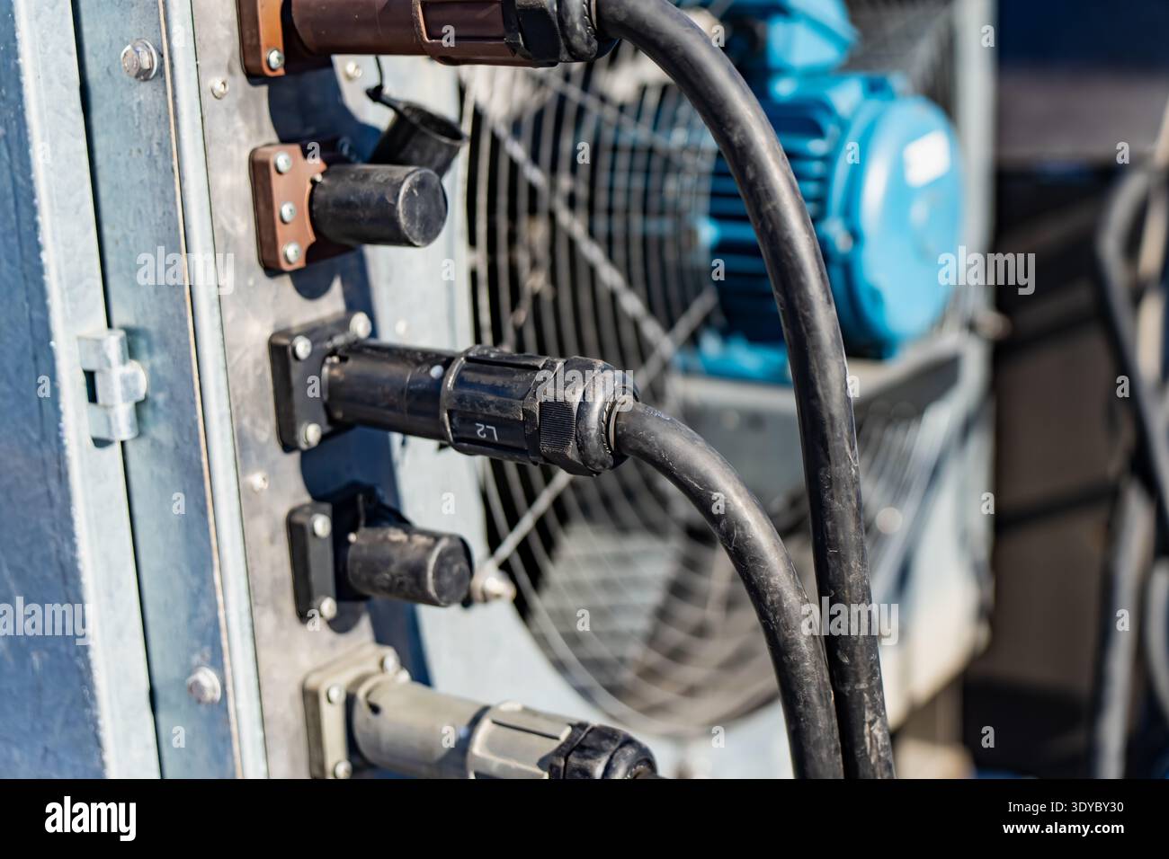 Câbles électriques robustes et connecteurs de verrouillage branchés sur le panneau de distribution électrique extérieur, cordons épais acheminés vers l'équipement équipé d'un ventilateur de refroidissement Banque D'Images