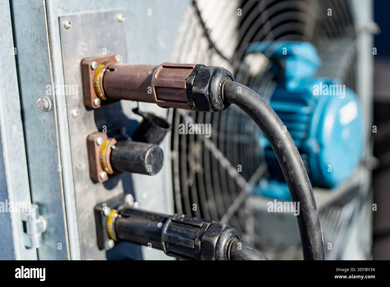 Fiche électrique robuste avec collier de verrouillage fileté connecté à l'armoire de commande métallique, câble noir courbé vers les machines, puissance industrielle Banque D'Images