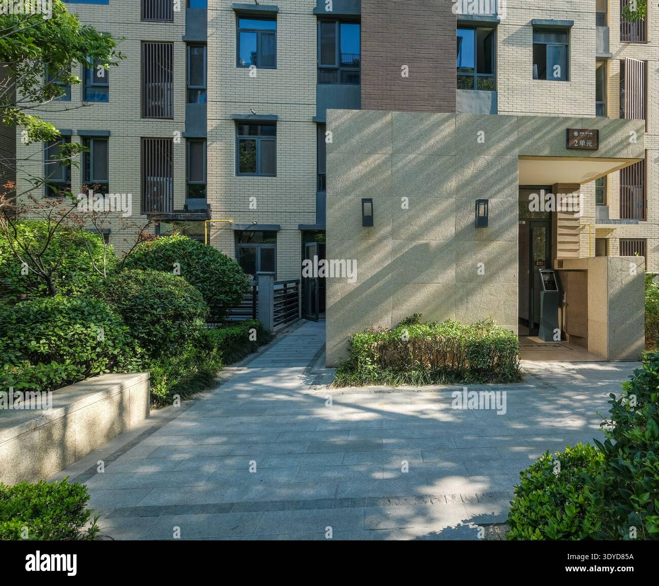 Une photo de paysage d'une entrée d'immeuble moderne avec un sol pavé de pierre et des haies bien entretenues dans un jardin communautaire serein. Banque D'Images