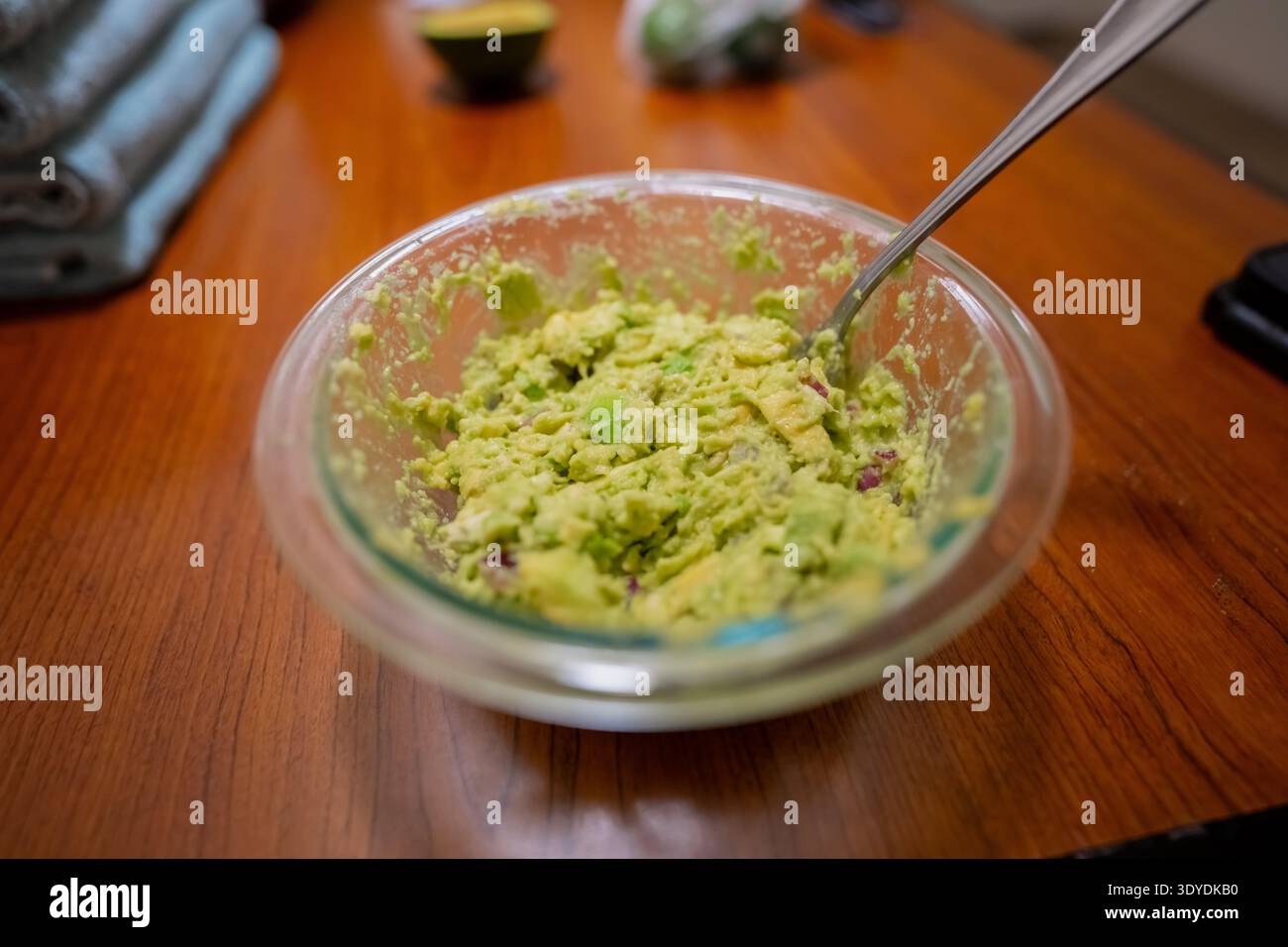 Guacamole maison fraîche dans un bol en verre clair sur une table en bois avec cuillère, mélange d'avocats en purée préparé pour les tacos, scène de cuisine saine dans la cuisine Banque D'Images