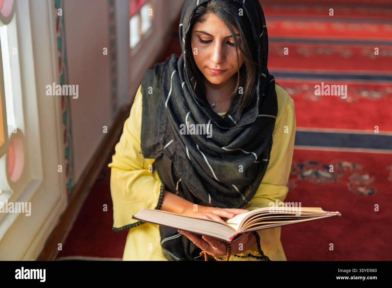 Une femme musulmane portant un foulard lit le Coran dans une mosquée. Banque D'Images