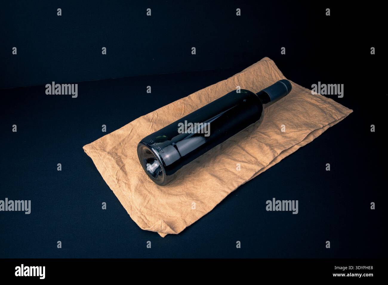 Bouteille de vin non étiquetée couchée sur une serviette en tissu au-dessus d'une surface sombre, photographiée avec une lumière sombre comme une nature morte minimaliste sur le service, la préparation Banque D'Images