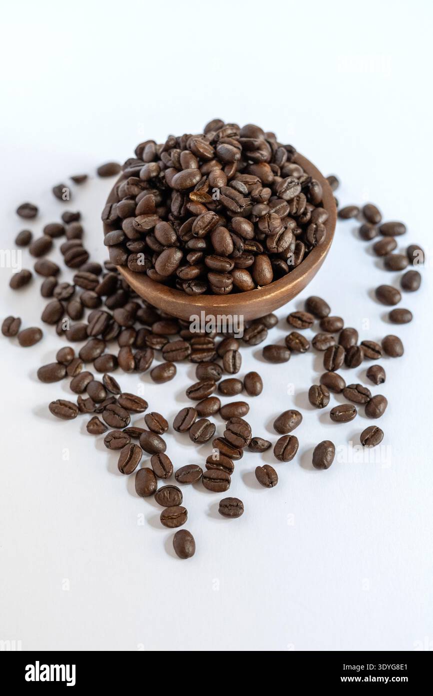 Une photographie verticale en grand angle de grains de café torréfiés foncés de qualité supérieure. Un petit bol en bois rustique est rempli de haricots et placé sur un sur blanc propre Banque D'Images