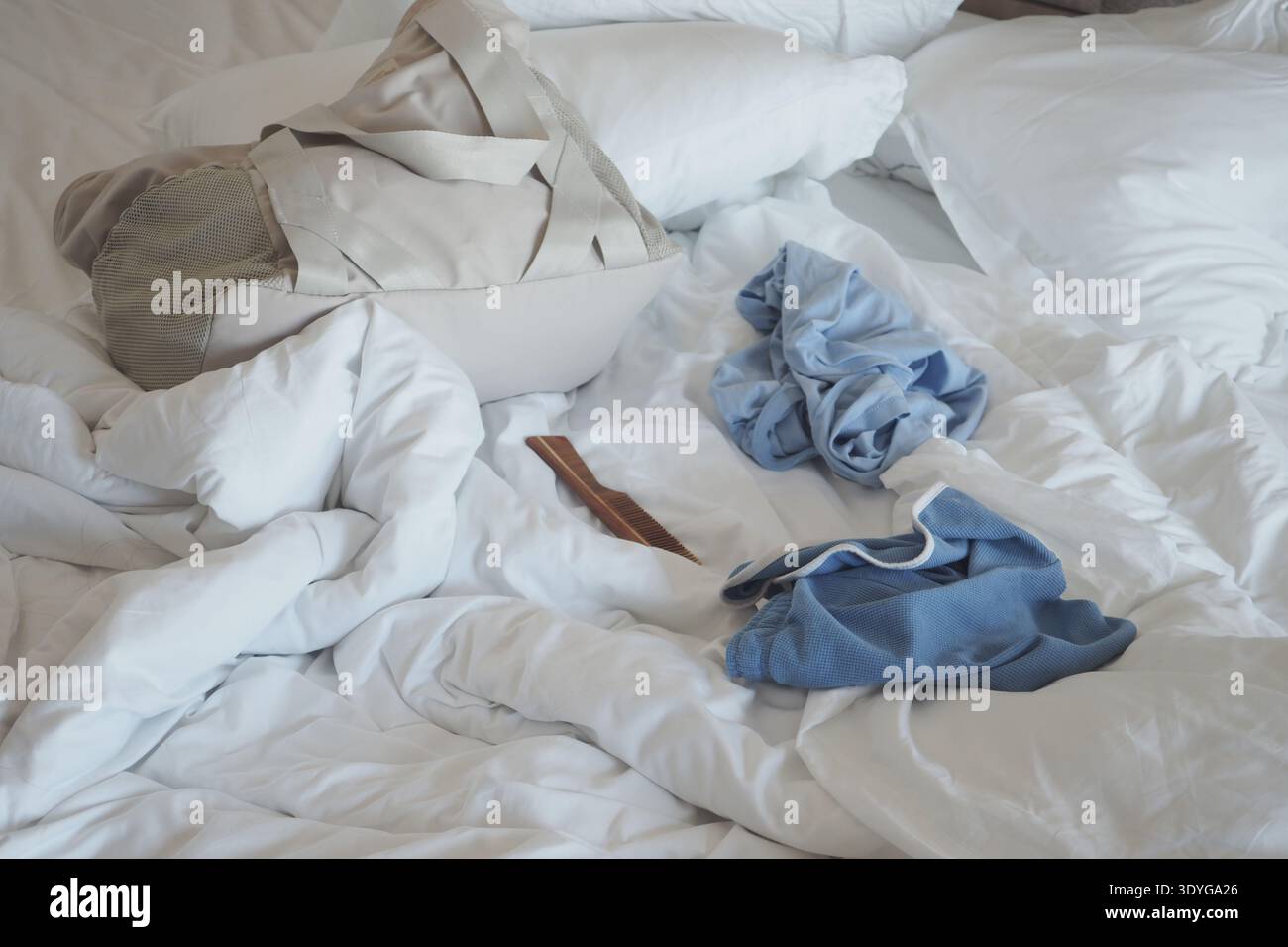 Vêtements et sac sur le lit en désordre avec des draps blancs Banque D'Images