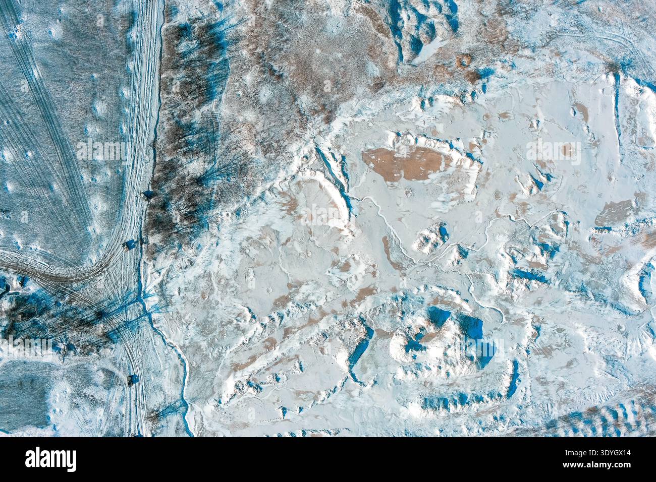 Cette fosse industrielle en argile recouverte de neige présente des lignes d'excavation profondes et des traces de pneus. Un paysage gelé d'extraction de ressources capture la dure réalité des opérations minières hivernales et des textures. Banque D'Images