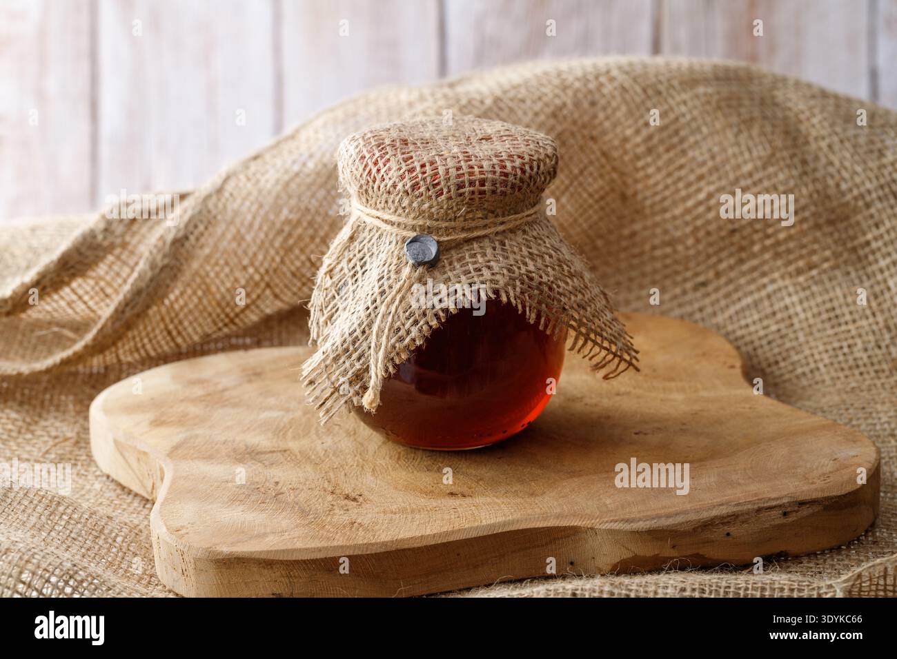 Pot en verre de miel de forêt naturelle brun foncé de récolte fraîche sur planche de bois sur sac de jute. Dessert bio sain. Gros plan sur le bocal de rodage des abeilles. Banque D'Images