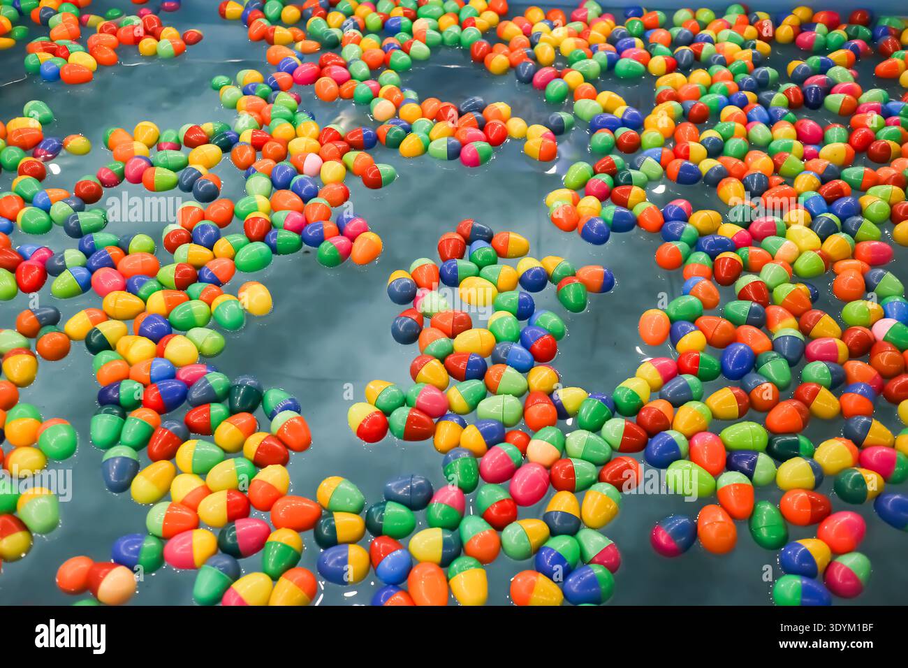 Boules en plastique colorées flottant sur l'eau dans un jeu équitable traditionnel, formant un fond abstrait vibrant avec une atmosphère de festival nostalgique. Banque D'Images