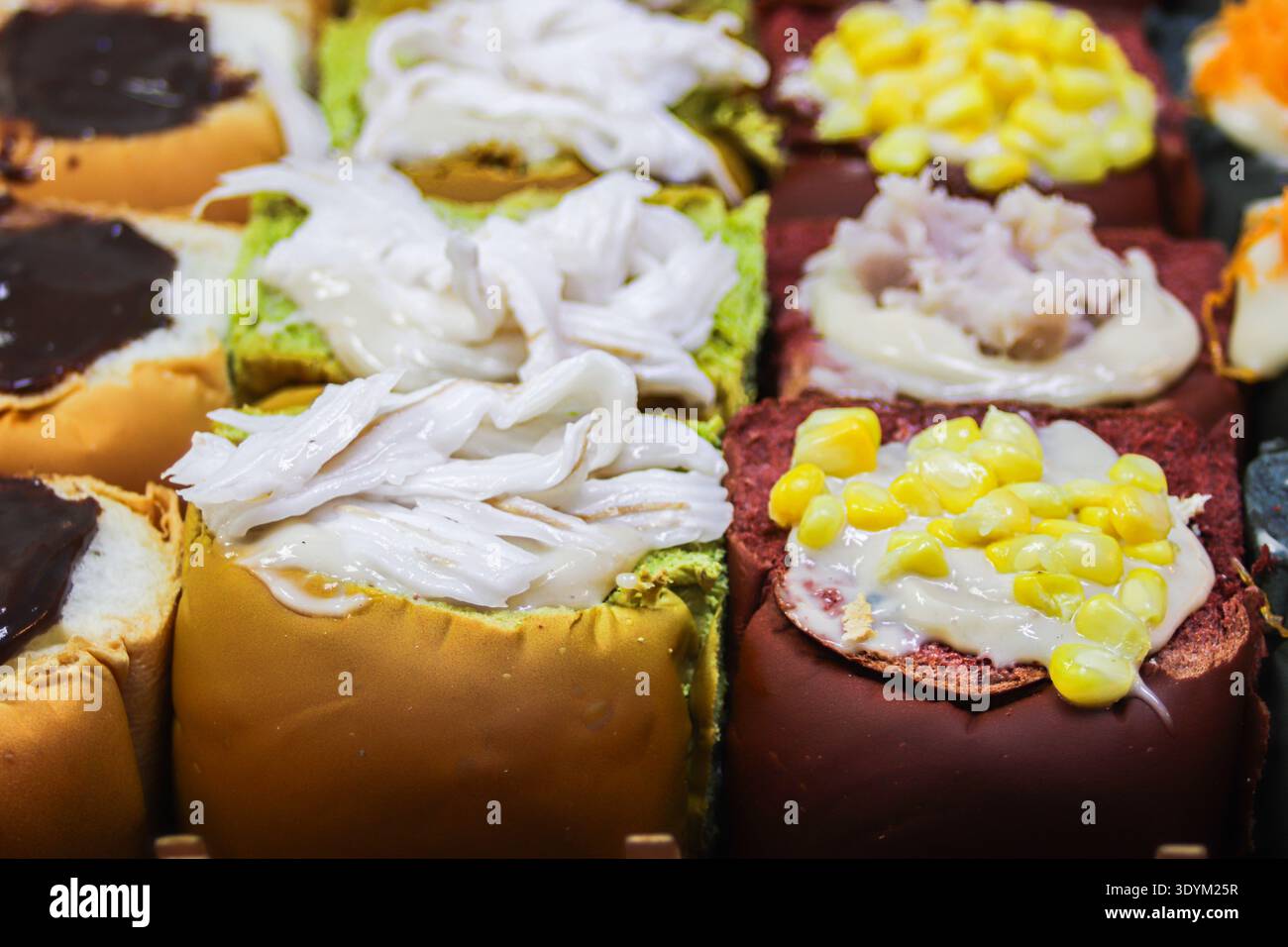 Petits pains fusion thaïlandais stylisés comme des sushis avec des garnitures de noix de coco, de maïs et de taro. Dessert de boulangerie coloré inspiré par la culture moderne de la Street food. Banque D'Images