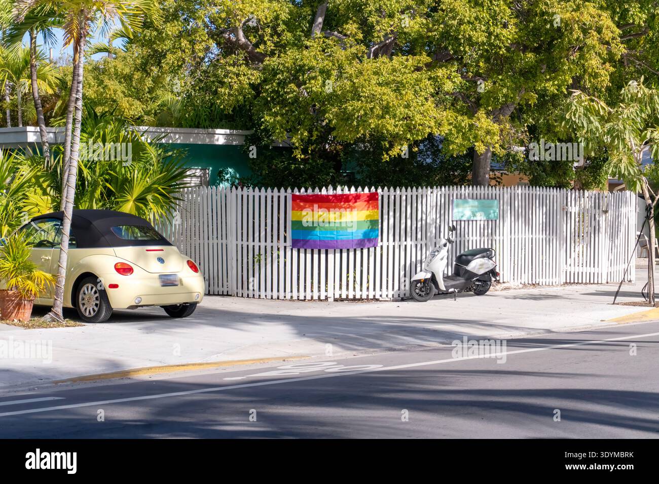 Cabriolet jaune et Scooter garés par une clôture de piquet blanc avec un drapeau Rainbow Pride à Key West Banque D'Images