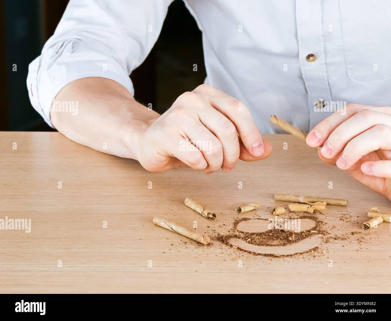 Vue rapprochée de mains cassant une cigarette en deux sur un visage heureux dessiné avec du tabac et des morceaux de cigarette sur bois, illustrant la joie de quitter smoki Banque D'Images