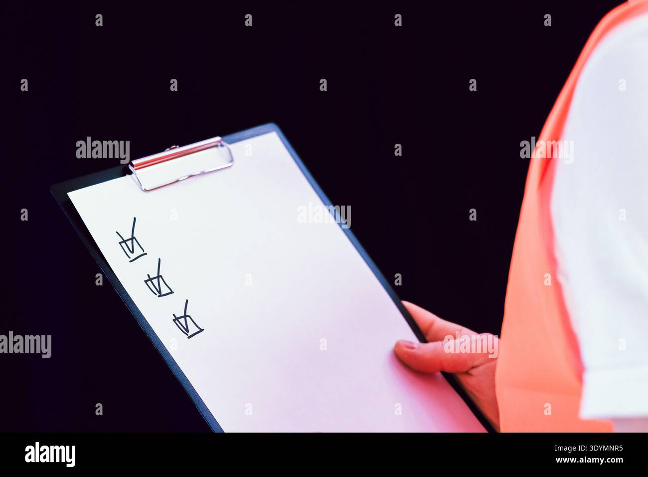 Vue latérale d'un ouvrier de la construction en gilet orange examinant le presse-papiers avec des éléments marqués de la liste de contrôle. Banque D'Images