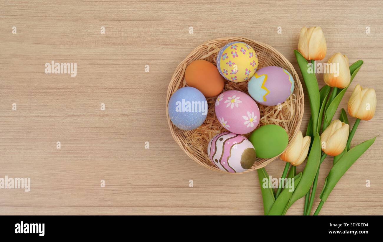 Panier de Pâques. Oeufs colorés et tulipes dans un panier sur fond de bois. Banque D'Images