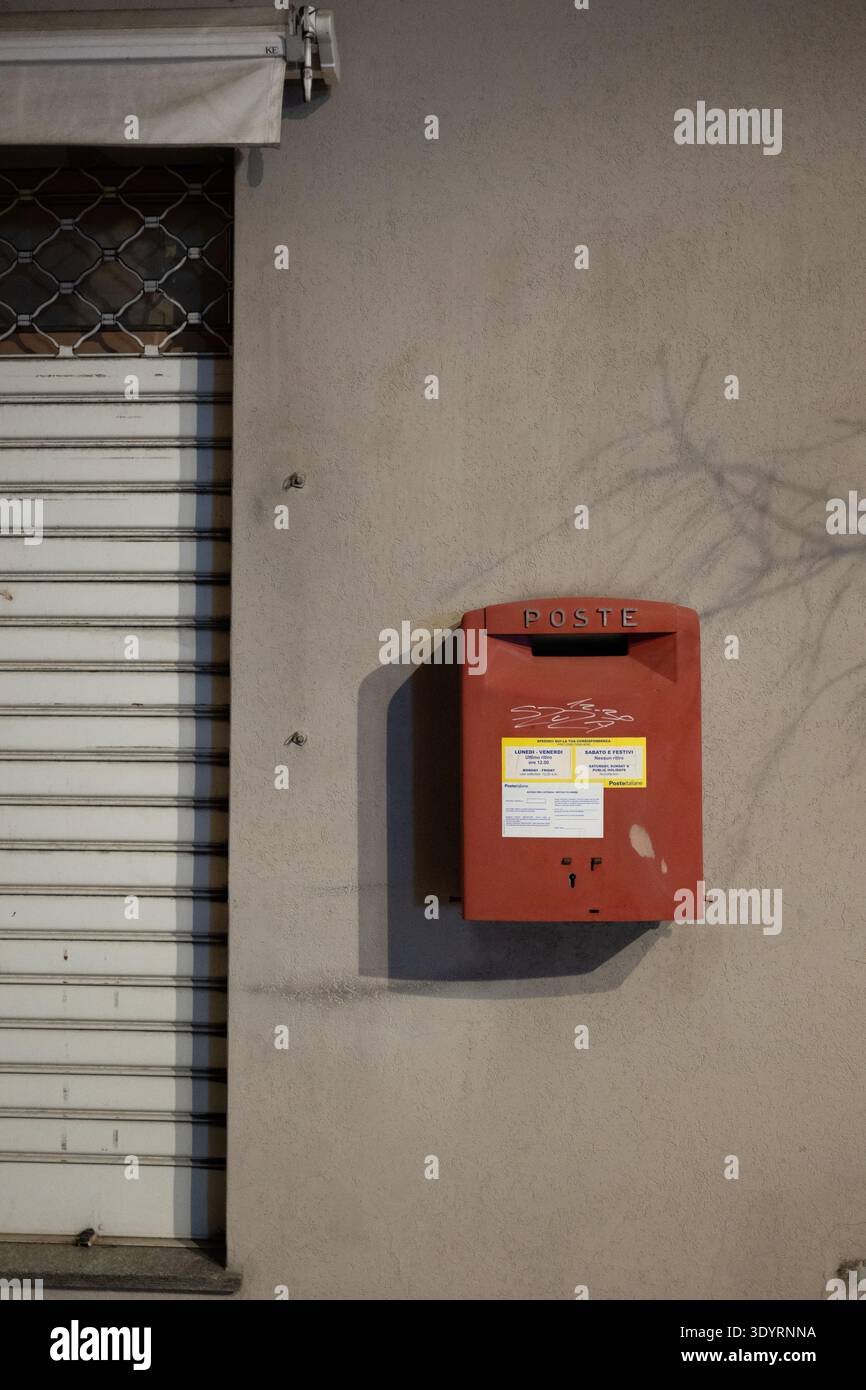 Boîte aux lettres murale rouge sur une façade de bâtiment urbain beige avec volet métallique. Banque D'Images