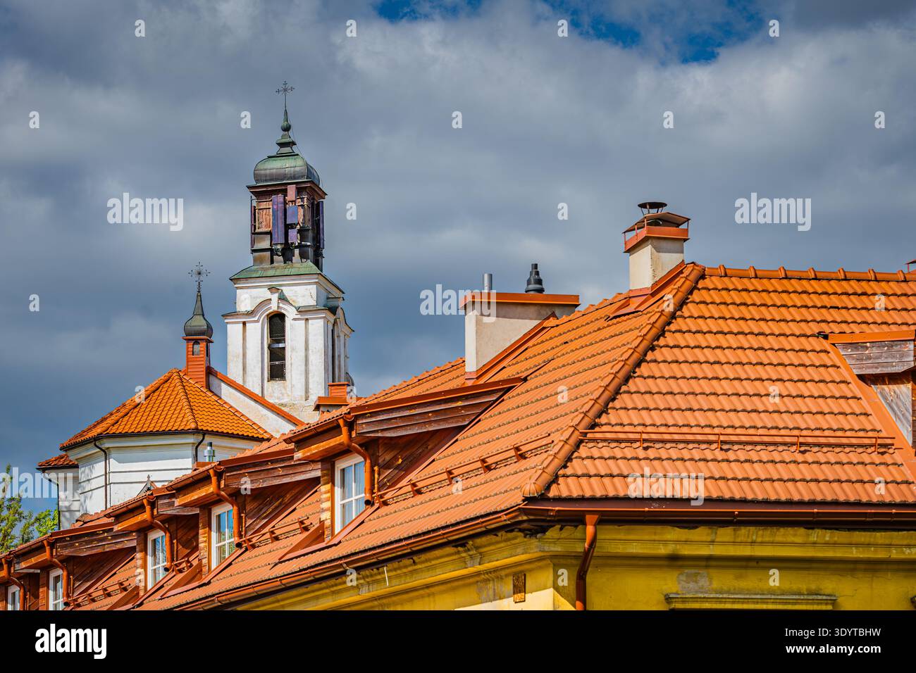 Gros plan des toits traditionnels en tuiles d'argile orange et d'un beffroi d'église blanc historique sous un ciel nuageux spectaculaire à Vilnius, Lituanie. Banque D'Images