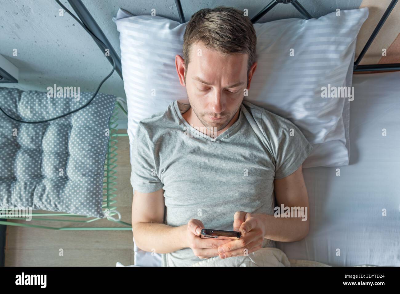 Homme couché dans le lit en utilisant un smartphone. Des lectures et des types masculins concentrés sur l'appareil tout en se reposant après le réveil. Habitudes numériques modernes. Technologie au quotidien Banque D'Images