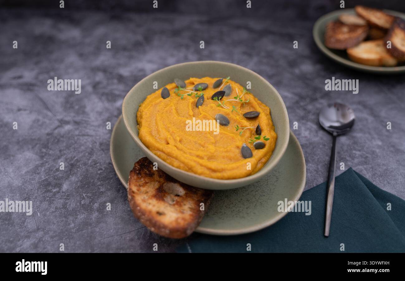 Soupe crémeuse à la citrouille servie avec du pain grillé et cuillère sur un bol vert sur une surface grise Banque D'Images