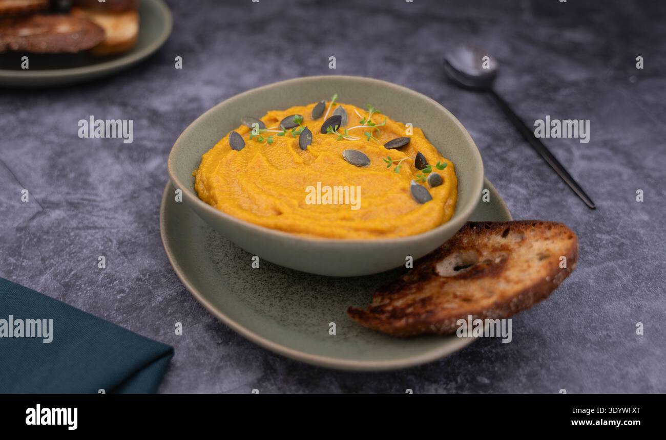 Bol de soupe à la citrouille garnie de graines servi avec du pain grillé sur la table grise Banque D'Images